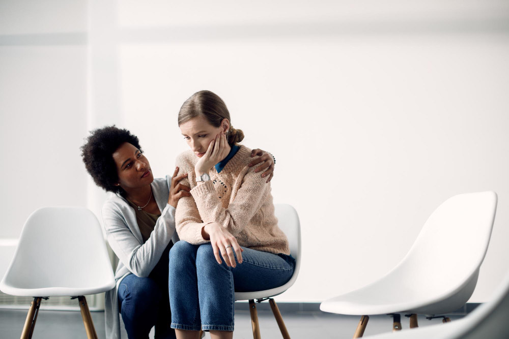 A clinician sitting with a client, a hand on her shoulder