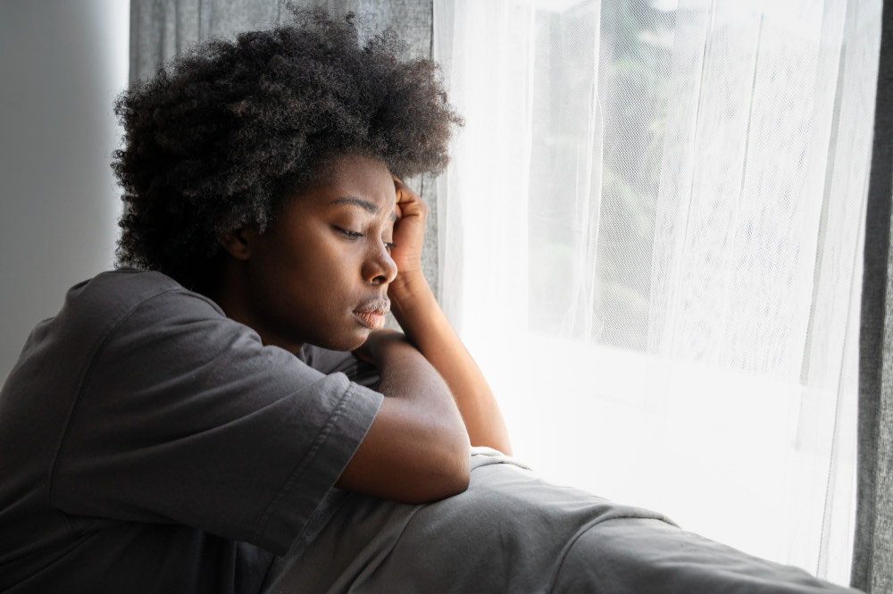 A young adult sitting alone at home, head lowered